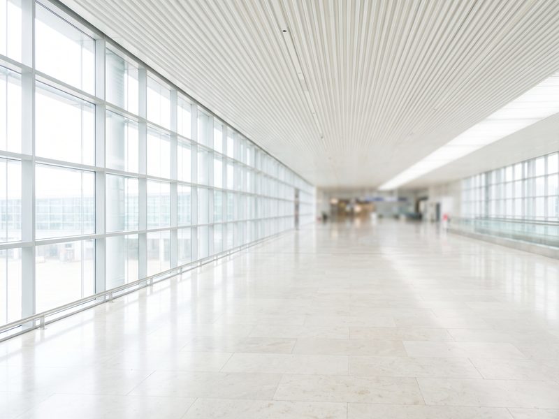 A bright airport terminal walkway with a glass curtain wall and a long clean sightline.