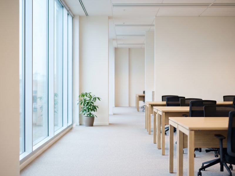 A bright Scandinavian open-plan office with empty desks and daylight from full-height windows.