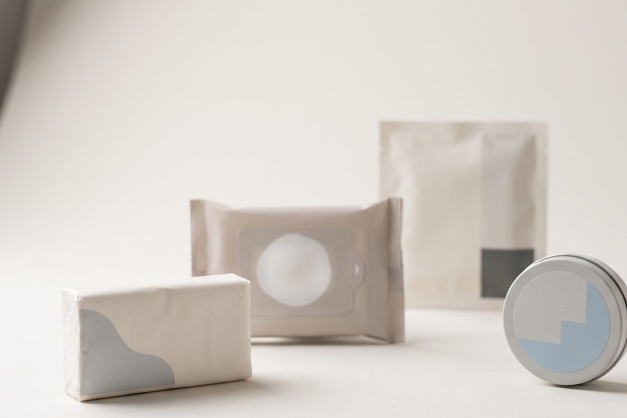 A pocket tissue pack, wet wipes, a sachet and a small tin arranged on a studio table.